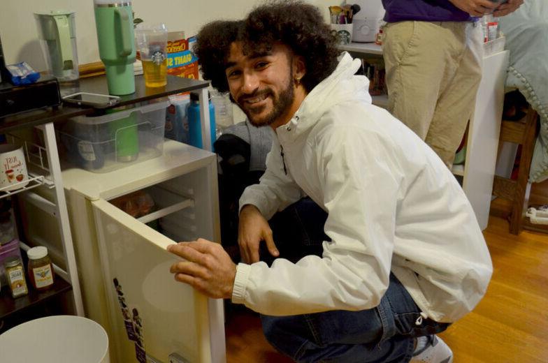 A male student smiles as he opens the mini refrigerator